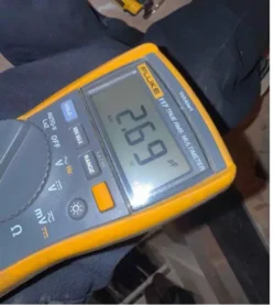 Digital multimeter measuring AC capacitor reading 26.9 microfarads, used to diagnose cooling problems