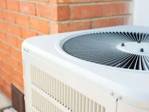 Outdoor HVAC condensing unit next to brick wall
