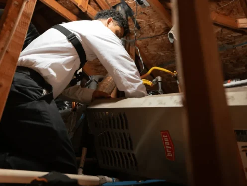 Technician servicing Bryant HVAC unit inside attic space